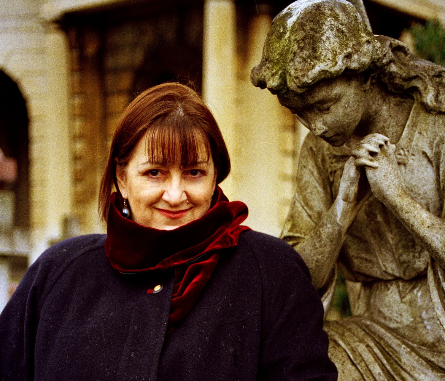 A woman in a coat standing next to a stone statue