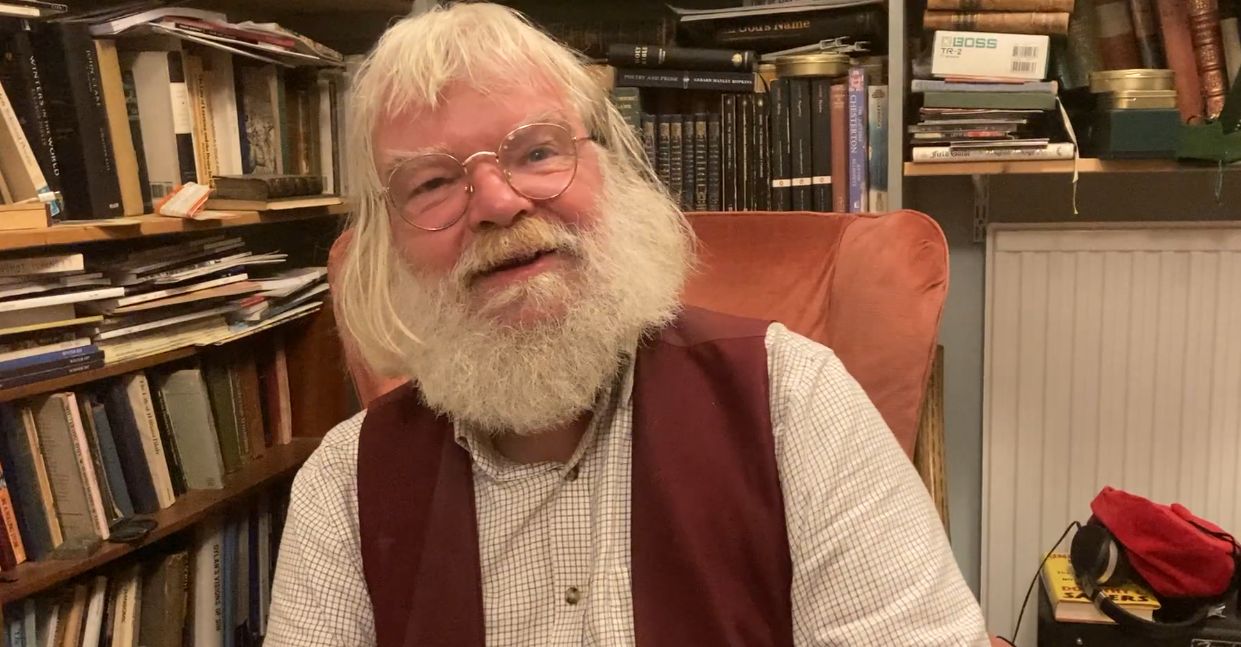 Man with a white beard seated in a chair with bookshelves in the background